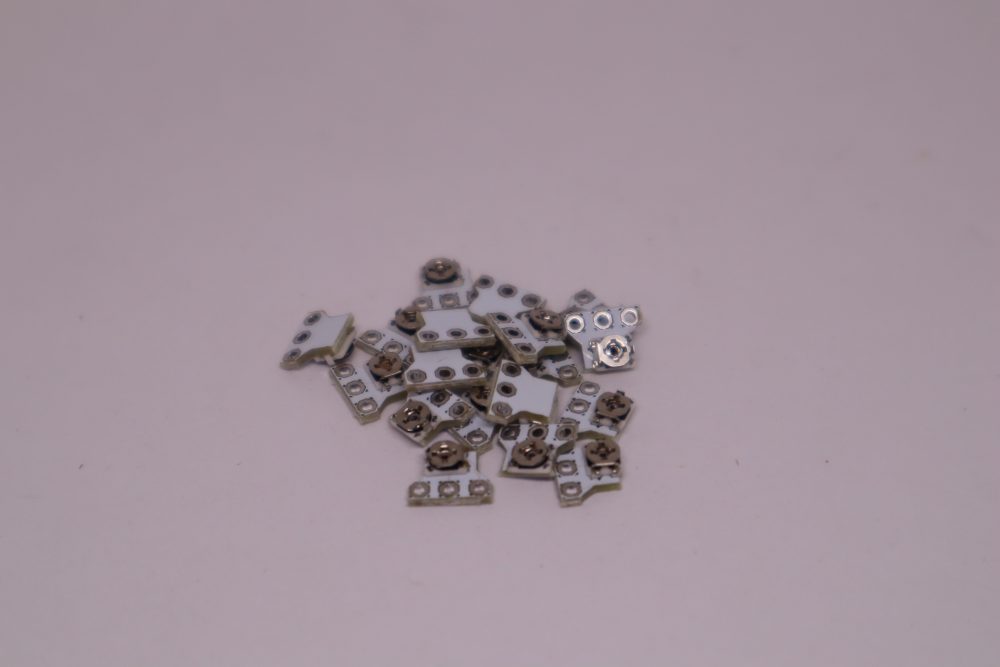 Ein kleiner Haufen metallischer Stick neu kalibrieren Modul-Komponenten ist auf einer hellrosa Oberfläche verstreut und erinnert an die winzigen Teile im Inneren eines PS5-Controllers.